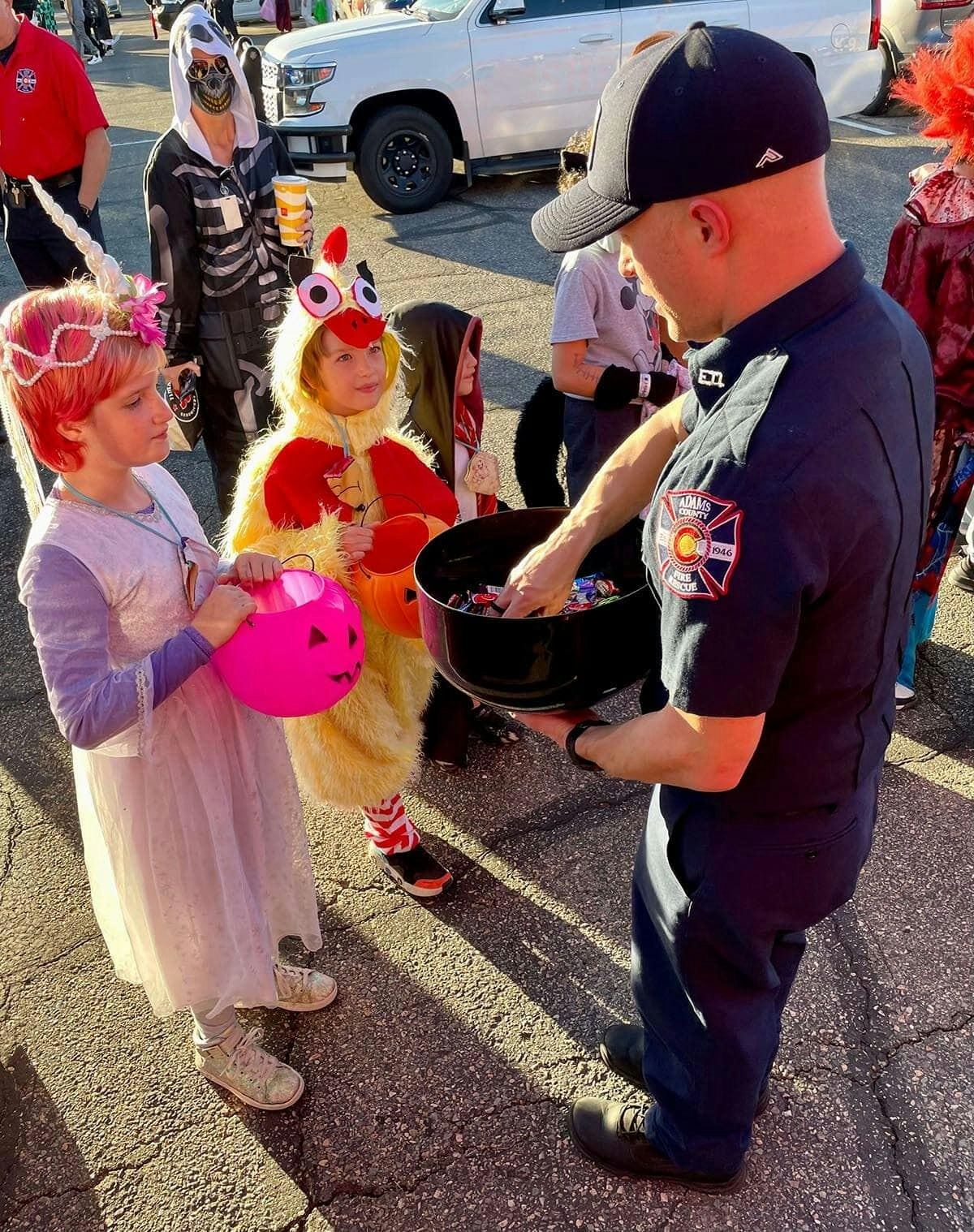 Kids in costumes are getting candy from a person in a uniform holding a large bowl during a Halloween event.