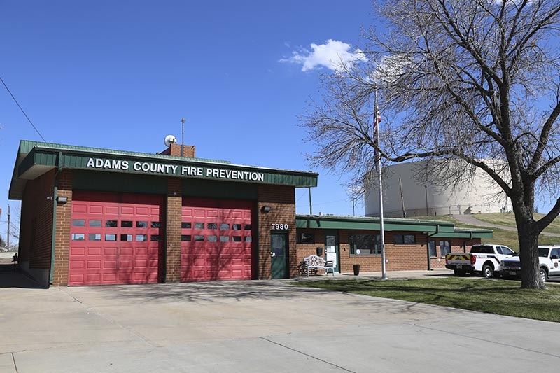 Adams County Fire Prevention building with two red garage doors, parked vehicles, and a tree.
