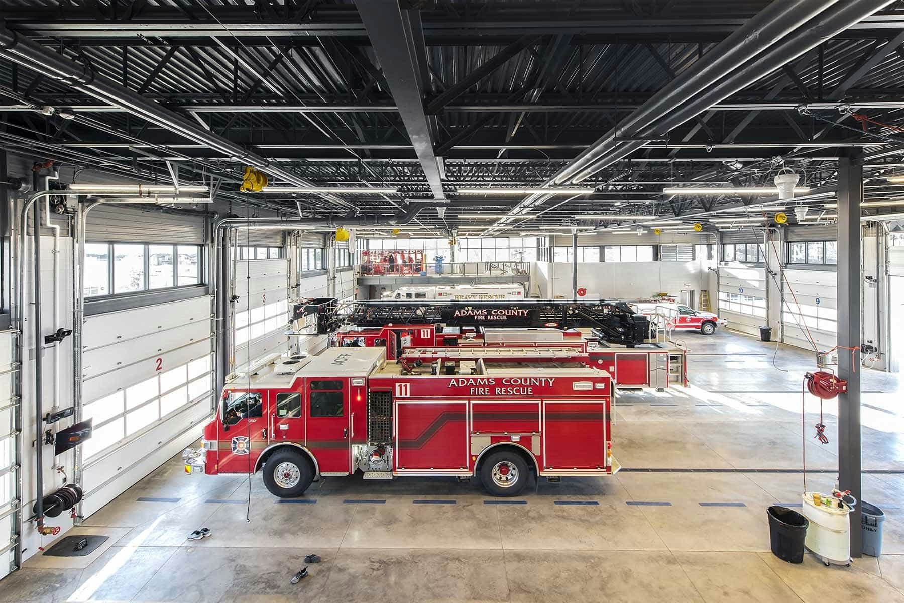 Fire station interior with several fire trucks, including "Adams County Fire Rescue" engines parked inside.