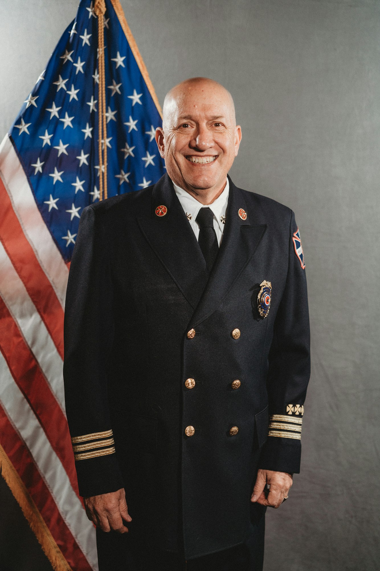 A smiling man in a uniform stands in front of the American flag.