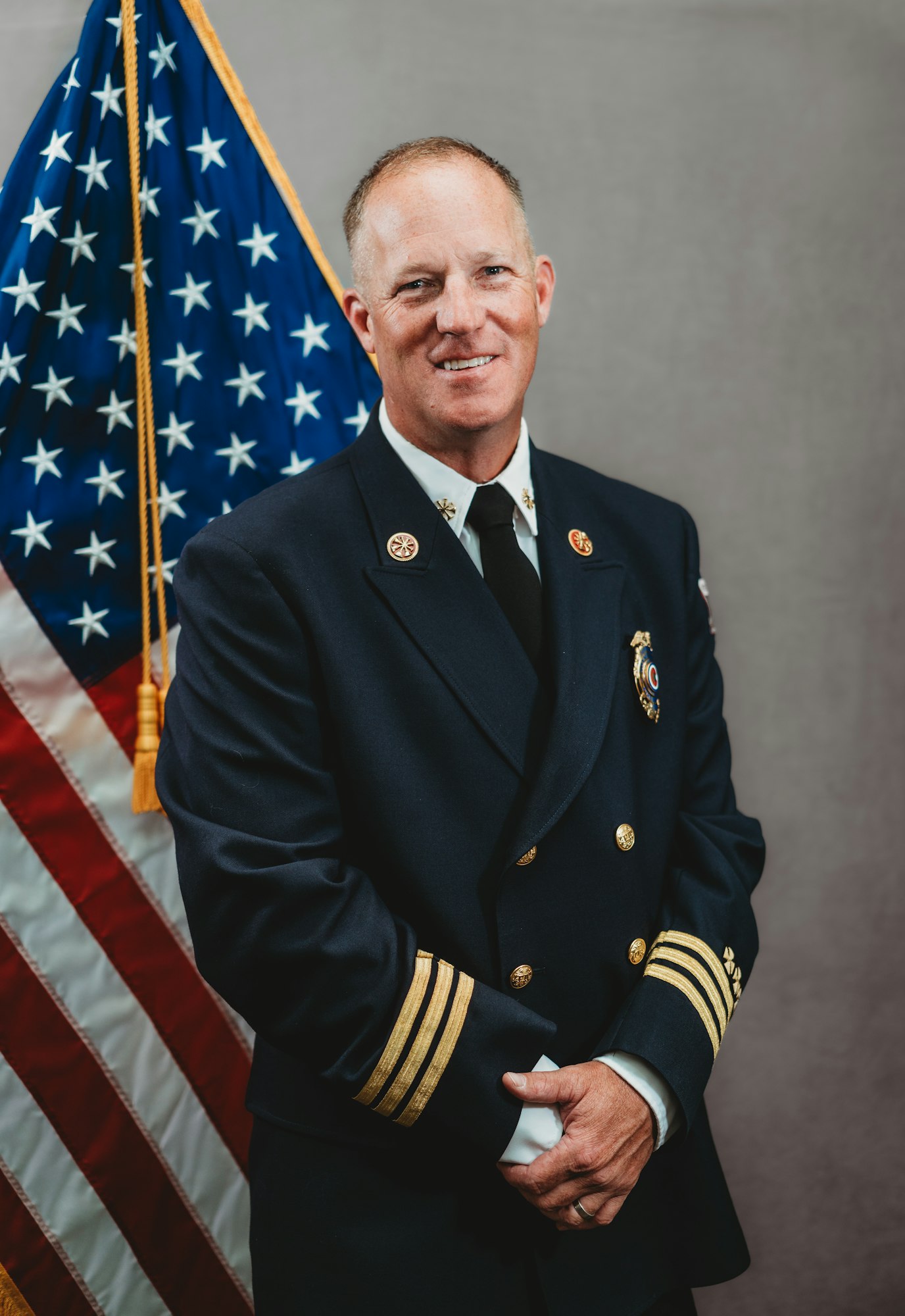 A person in a formal uniform stands in front of an American flag.