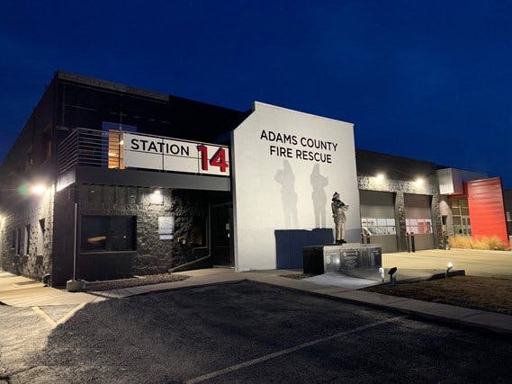Adams County Fire Rescue Station 14 building at night, with lights on and a memorial statue outside.