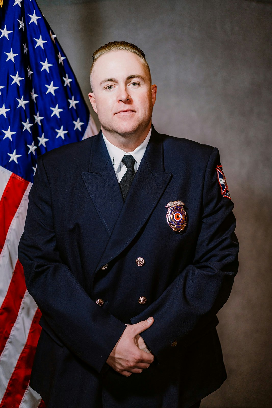 A person in a formal uniform stands in front of the U.S. flag.