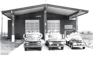 Three vintage fire trucks parked in front of a fire station.
