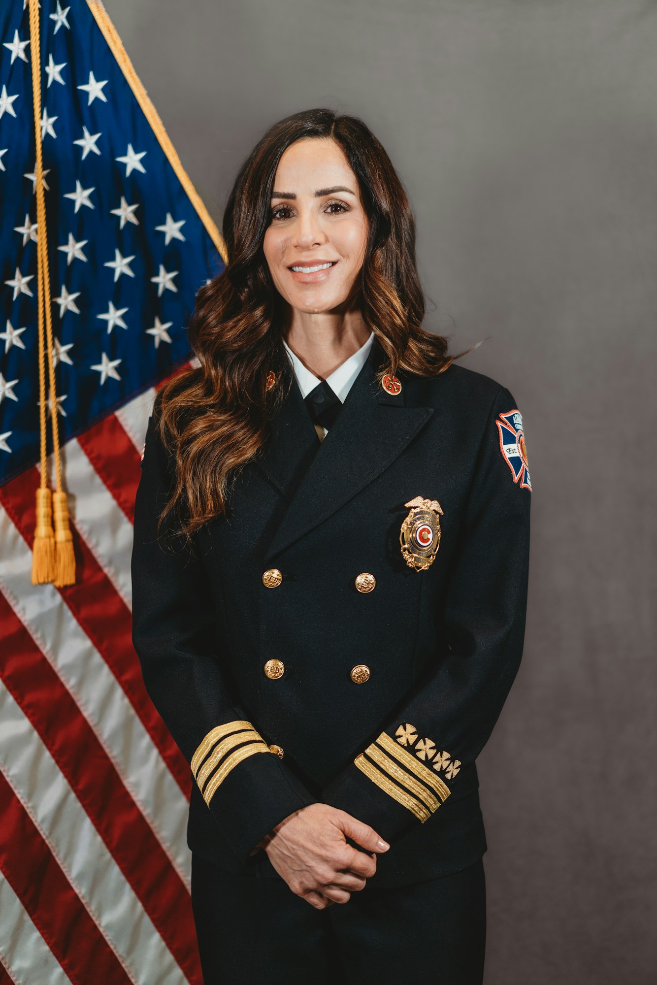 A person in a formal fire department uniform stands in front of a U.S. flag.