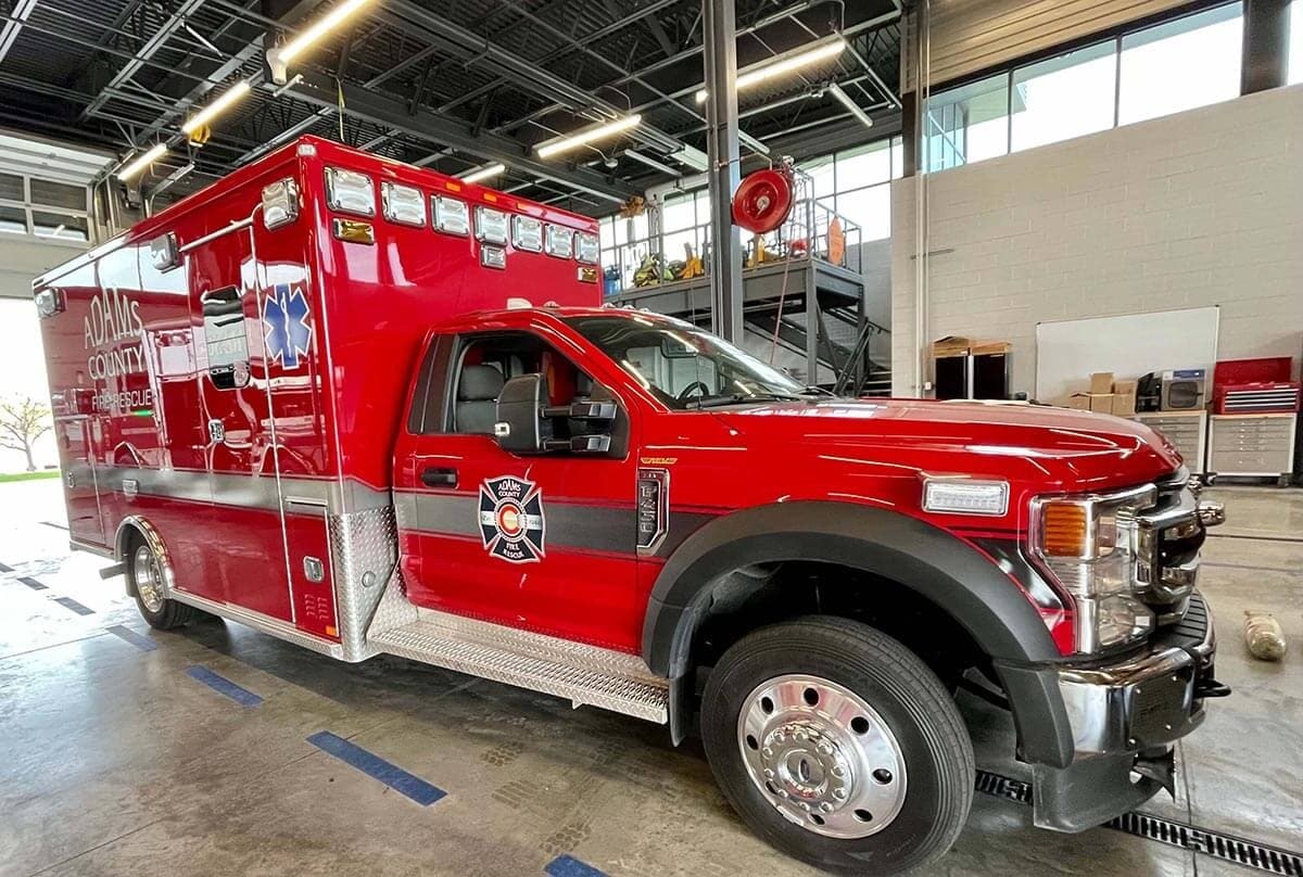 A red Adams County fire rescue ambulance parked inside a garage.