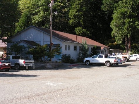 Outside view of Community building with some vehicles parked near it. Trees in background.