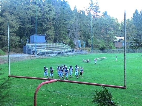 Looking over goalpost at Dunsmuir High School football team, grass, new grandstand and trees in background.