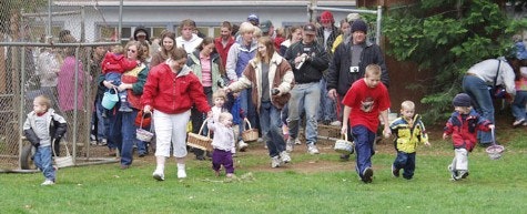 Ball Field on Easter Egg hunt. A few adults and lots of young children with baskets to collect eggs in grass.