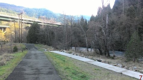 Tauhindauli Park foot trail with paved ramp to river for wheel chairs. trees along river and mountains in background