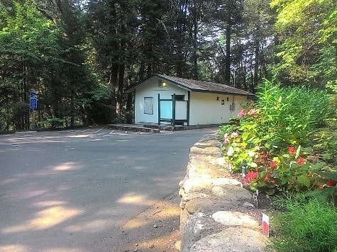 Looking across road with a rock lined garden on right and trees in background. Focal point is the lower park ADA restrooms..