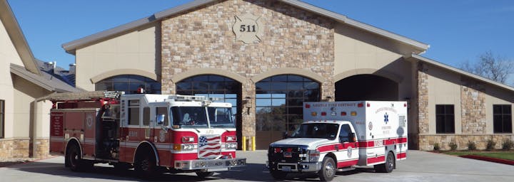 A firetruck and ambulance are parked in front of a fire station with a stone facade, marked with "511."