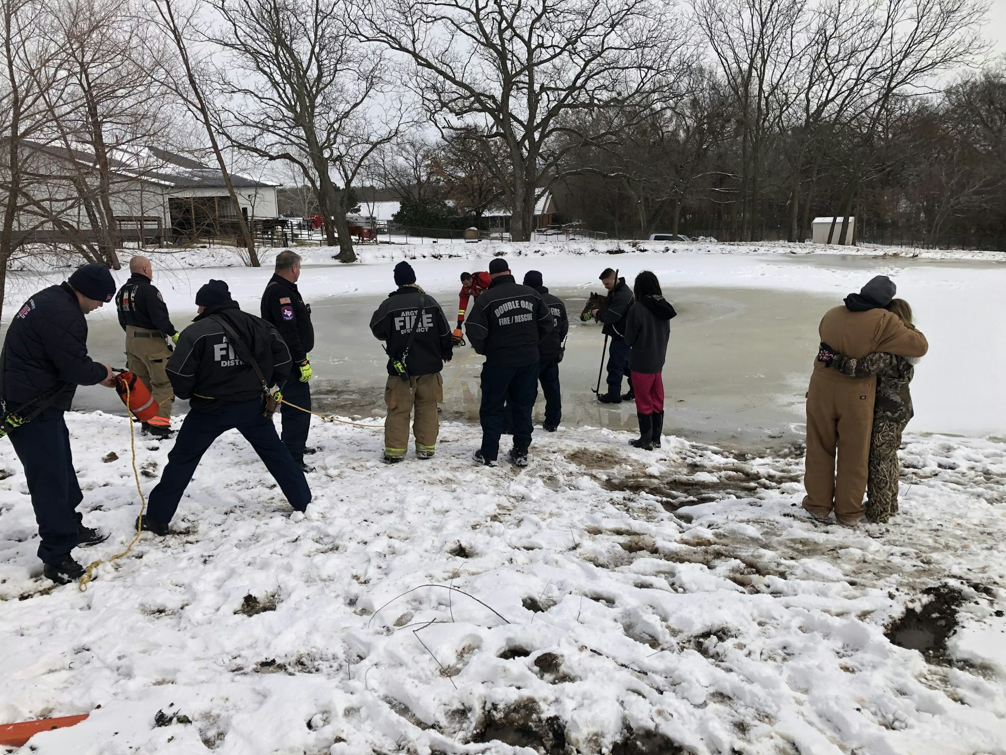 Rescue team at a snowy icy pond with onlookers nearby, preparing for possible action.