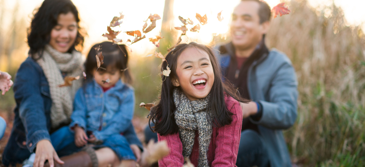 A family enjoying an autumn day, with leaves falling around them and children playing happily.
