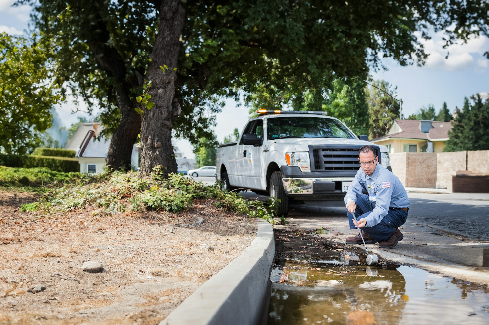 A worker is testing water in a puddle on a street beside a utility truck.