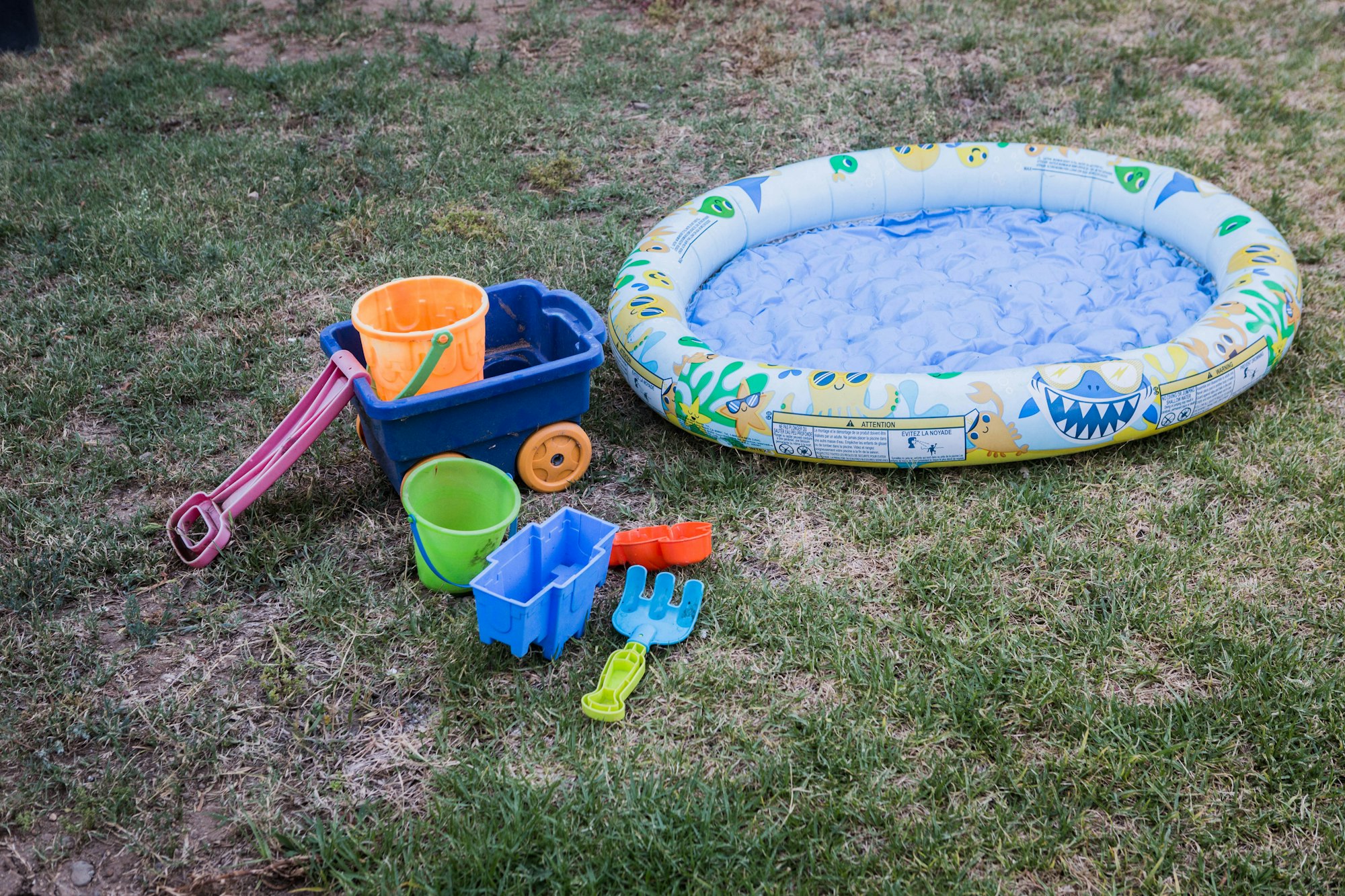 Inflatable kiddie pool and plastic toys, including buckets and shovels, on grass.