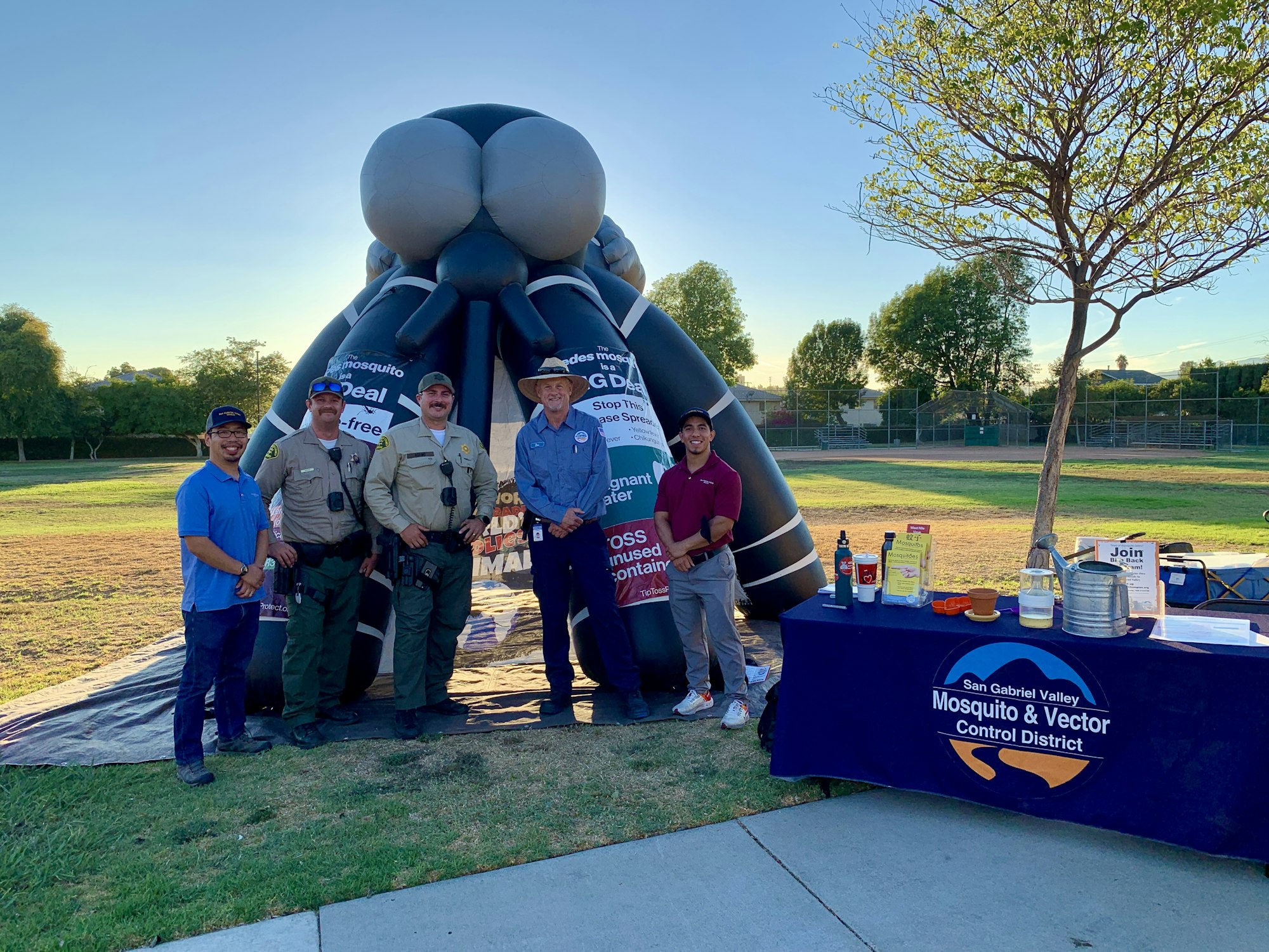 People at an outdoor event with an inflatable mosquito, educational materials, and a banner for mosquito control.