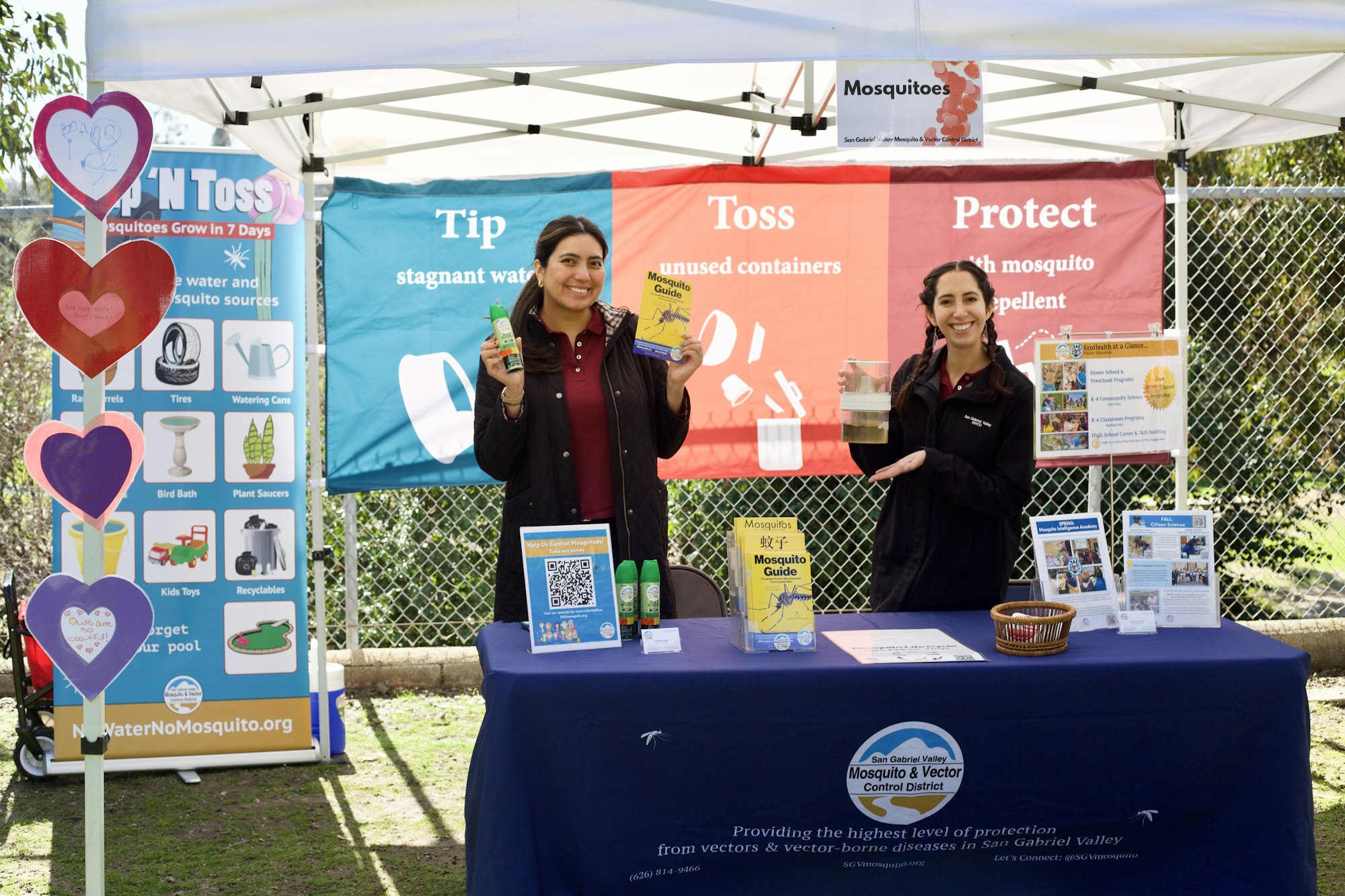 Two individuals at an educational booth about mosquito prevention, with informational banners and displays.