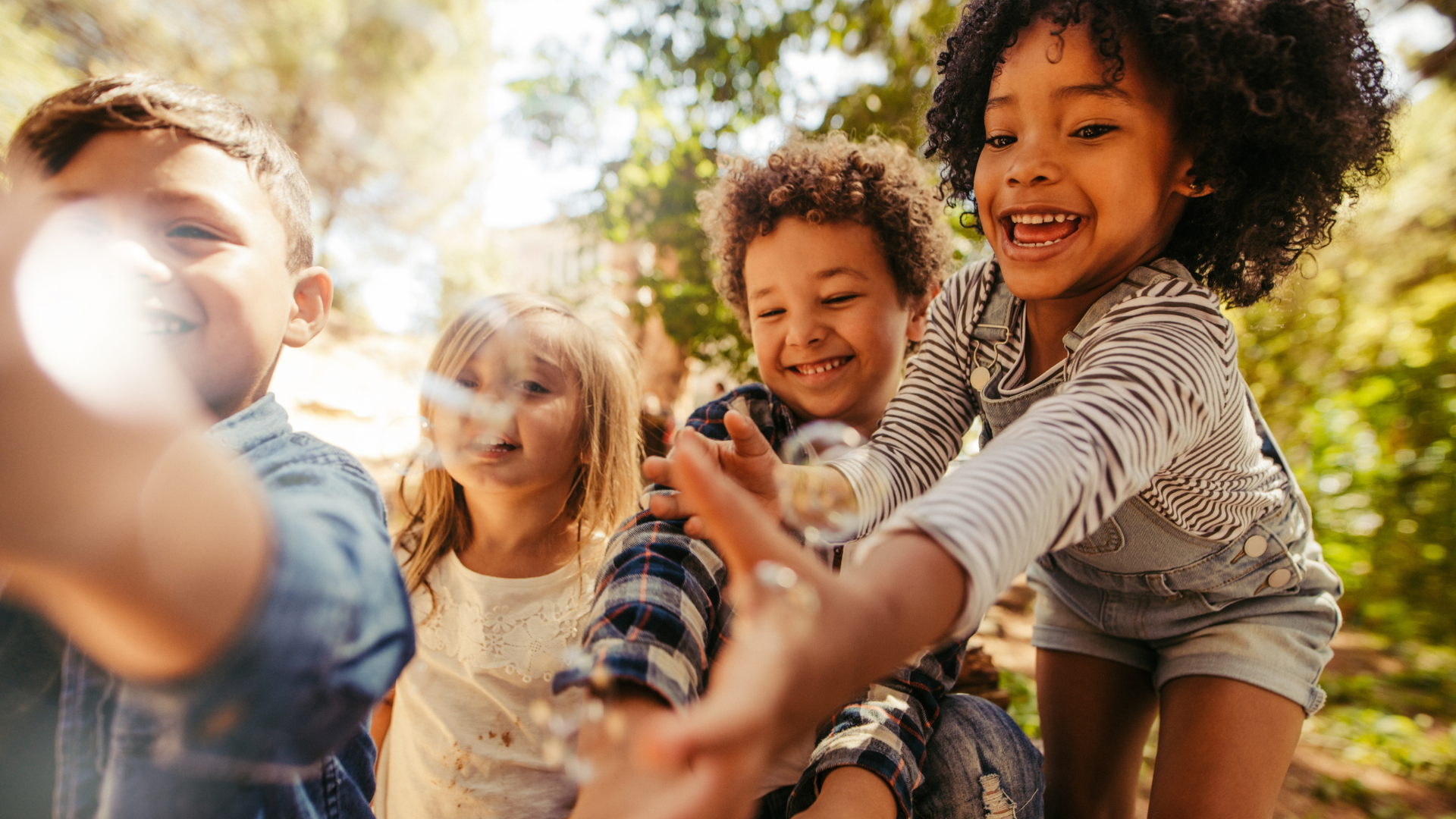 A group of happy children playing outside, reaching for bubbles with joyful expressions.