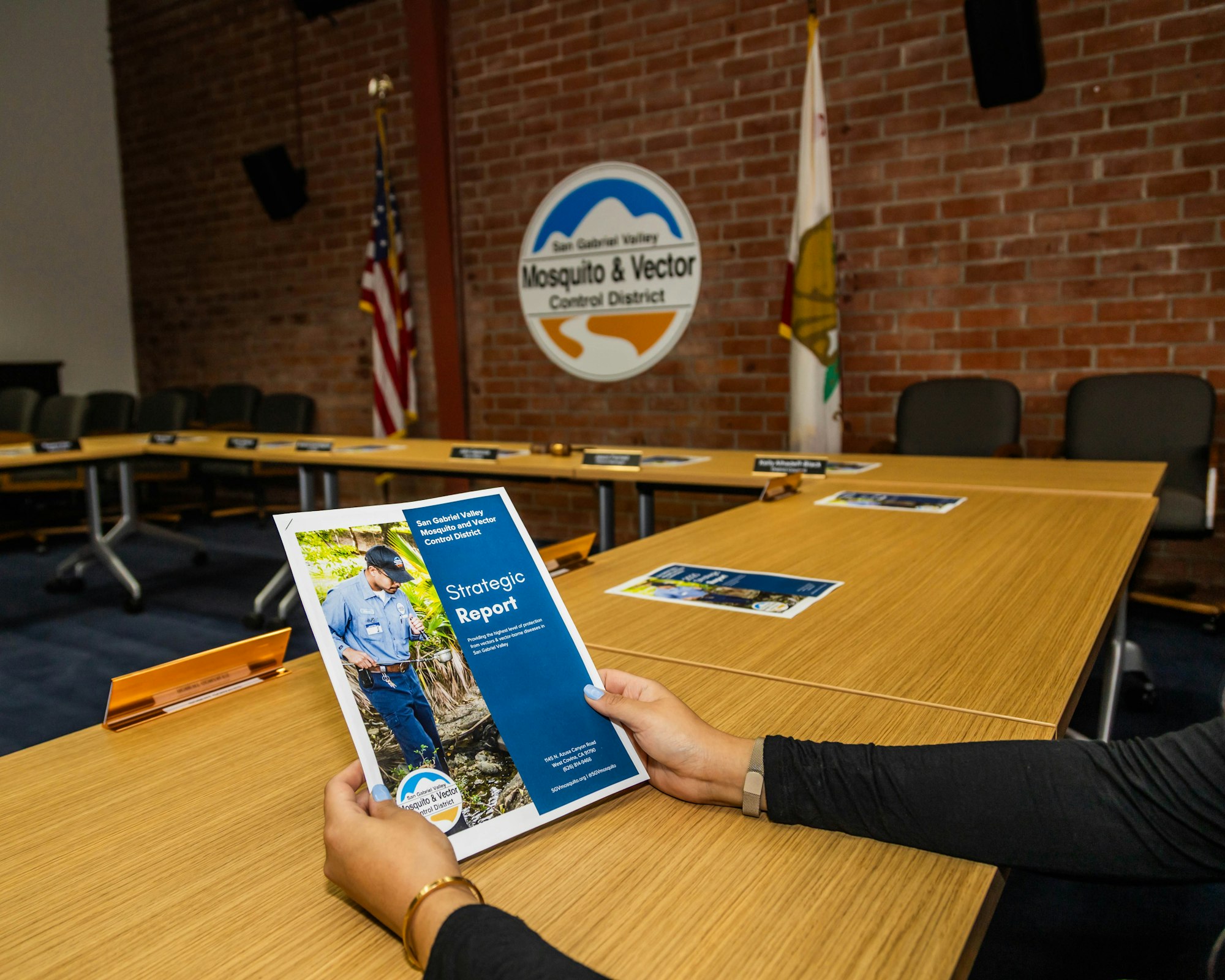 A person holds a "Strategic Report" for the San Gabriel Valley Mosquito & Vector Control District in a meeting room.