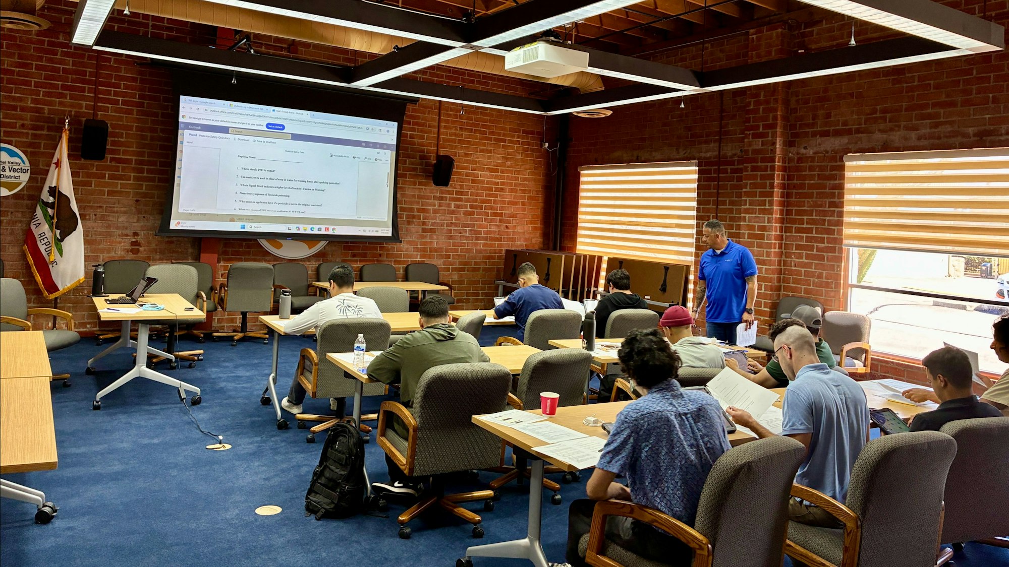 A classroom setting with students focused on a presentation, discussing documents, and a speaker leading the session.