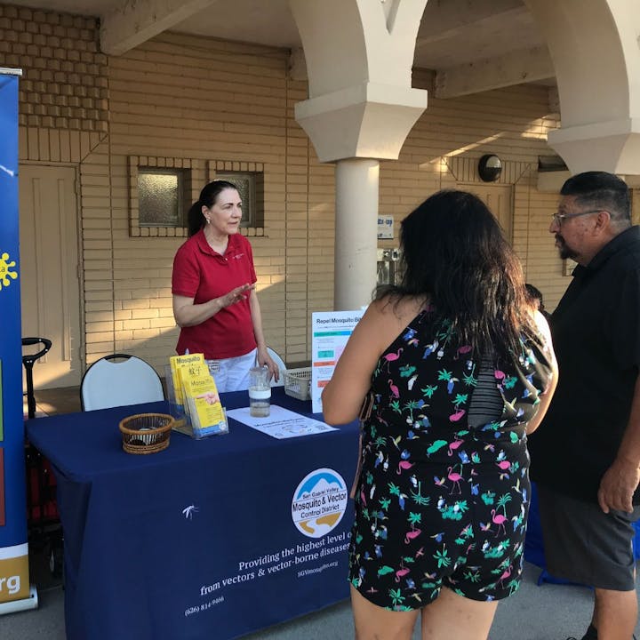 An information booth with a woman speaking to visitors about mosquito control and vector-borne diseases.