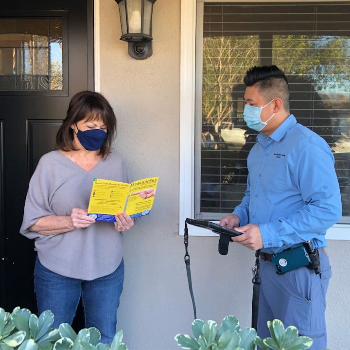 Two people wearing masks, one reading a brochure and the other holding a tablet, potentially discussing a service or information.