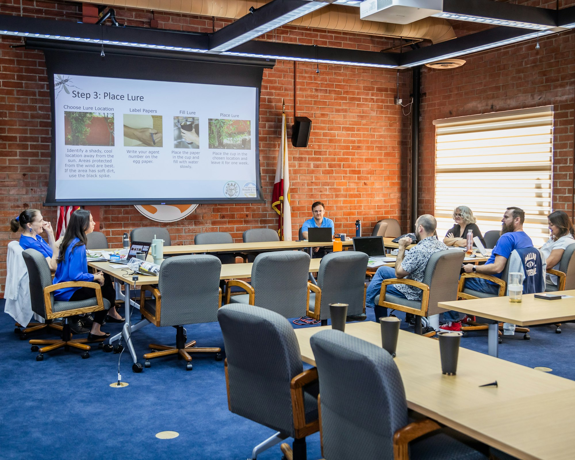 A group of people in a meeting room with a presentation on a screen.