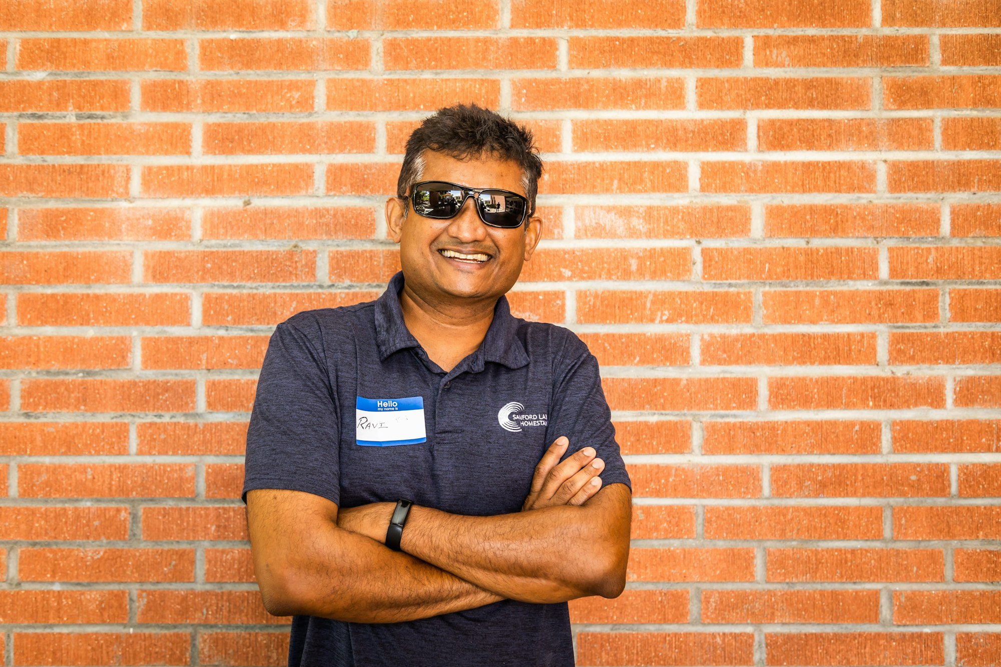 May contain: smile, person, head, face, happy, brick, portrait, photography, sunglasses, accessories, man, adult, male, wall, building, and architecture