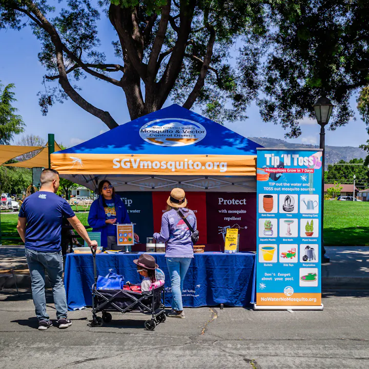 A community booth promoting mosquito control with tips, a rep, and a "Tip 'N Toss" initiative to eliminate standing water.