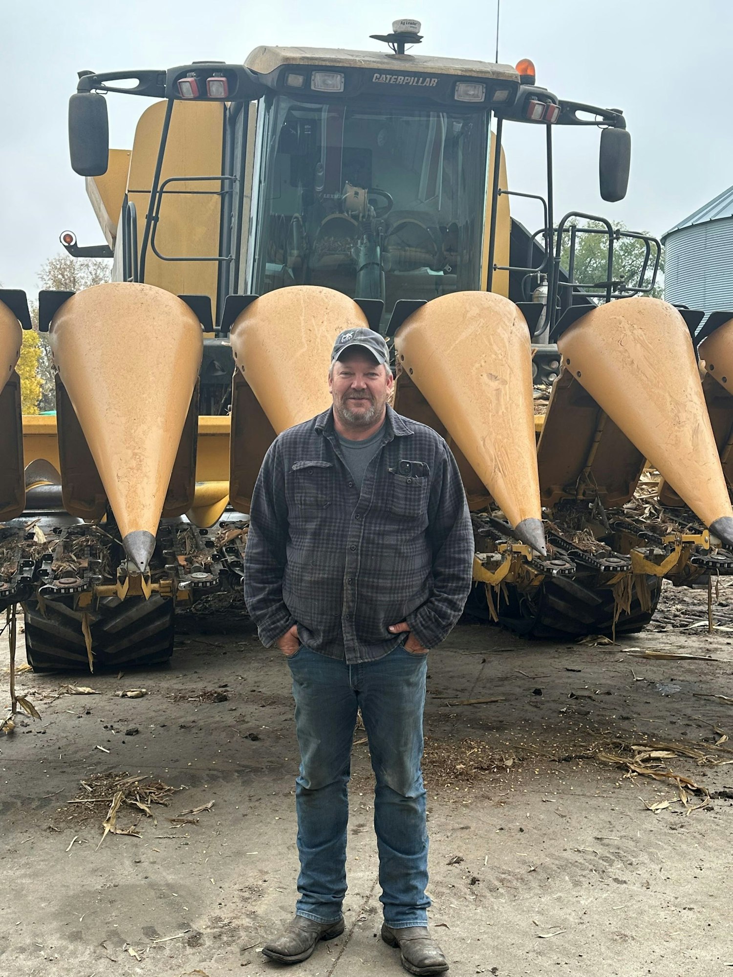 Man standing in front of a large yellow Caterpillar combine harvester.