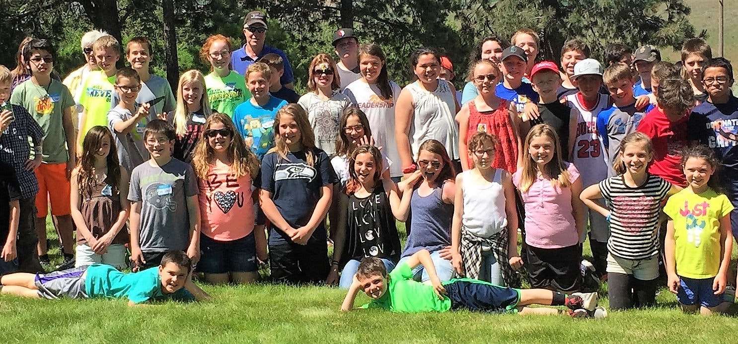 A large group of people, mostly children, pose outdoors on grass, standing and lying down.