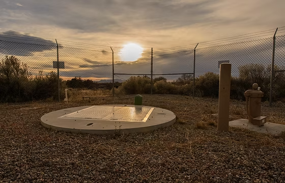 Fenced area with a circular concrete hatch, a fire hydrant, and a sunset in the background.
