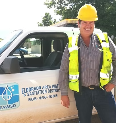A person wearing a yellow hard hat and safety vest stands next to a utility vehicle with "Eldorado Area Water & Sanitation District" on it.