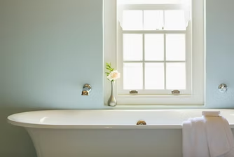 Freestanding bathtub with a towel, under a window with a vase and flower.