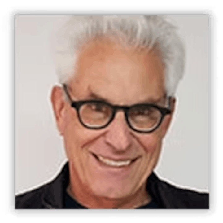 A smiling man with white hair and glasses wearing a dark jacket.