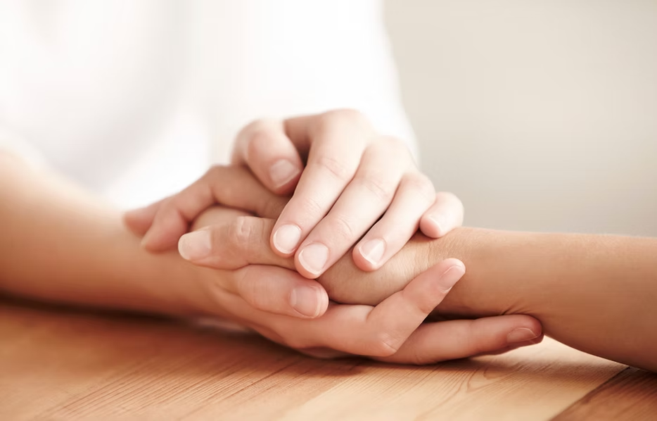 Two hands clasping another hand gently on a wooden surface, symbolizing support and care.