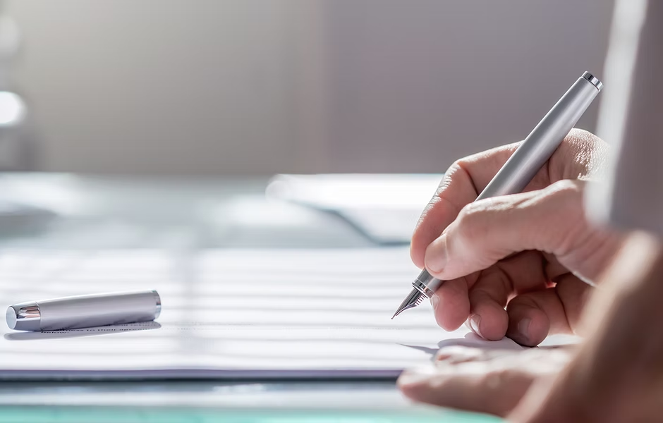 A hand writing with a fountain pen on paper, pen cap resting nearby.