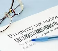 A property tax notice with a barcode, a pair of glasses, and a blue pen.