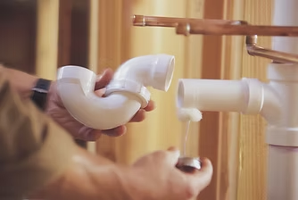 Person holding plumbing pipe parts near a wall, preparing to connect them.