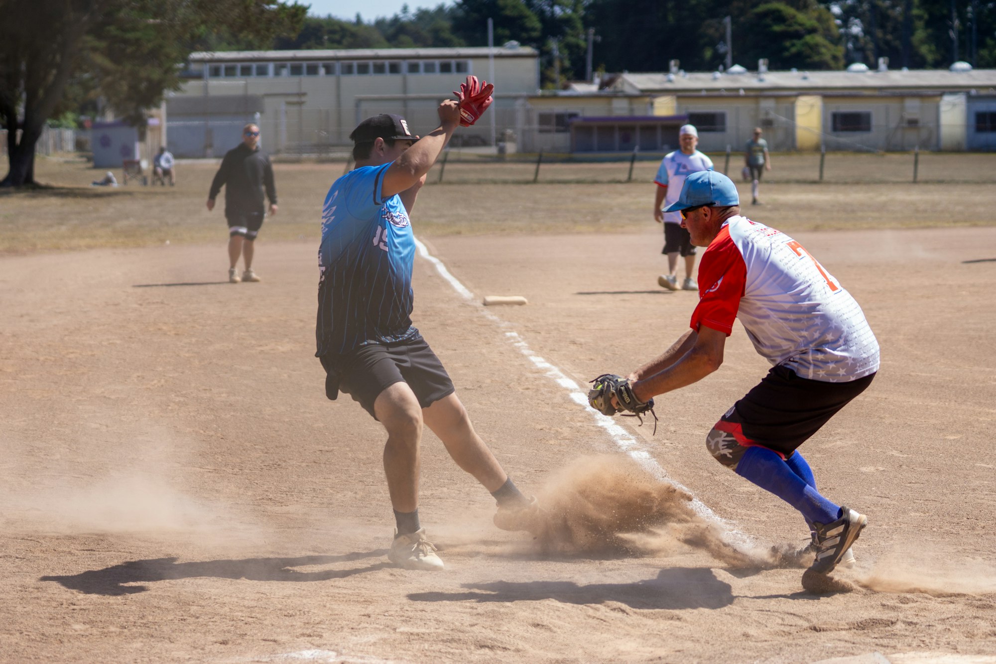 Two baseball players clash at a base, kicking up dust on a sunny field.