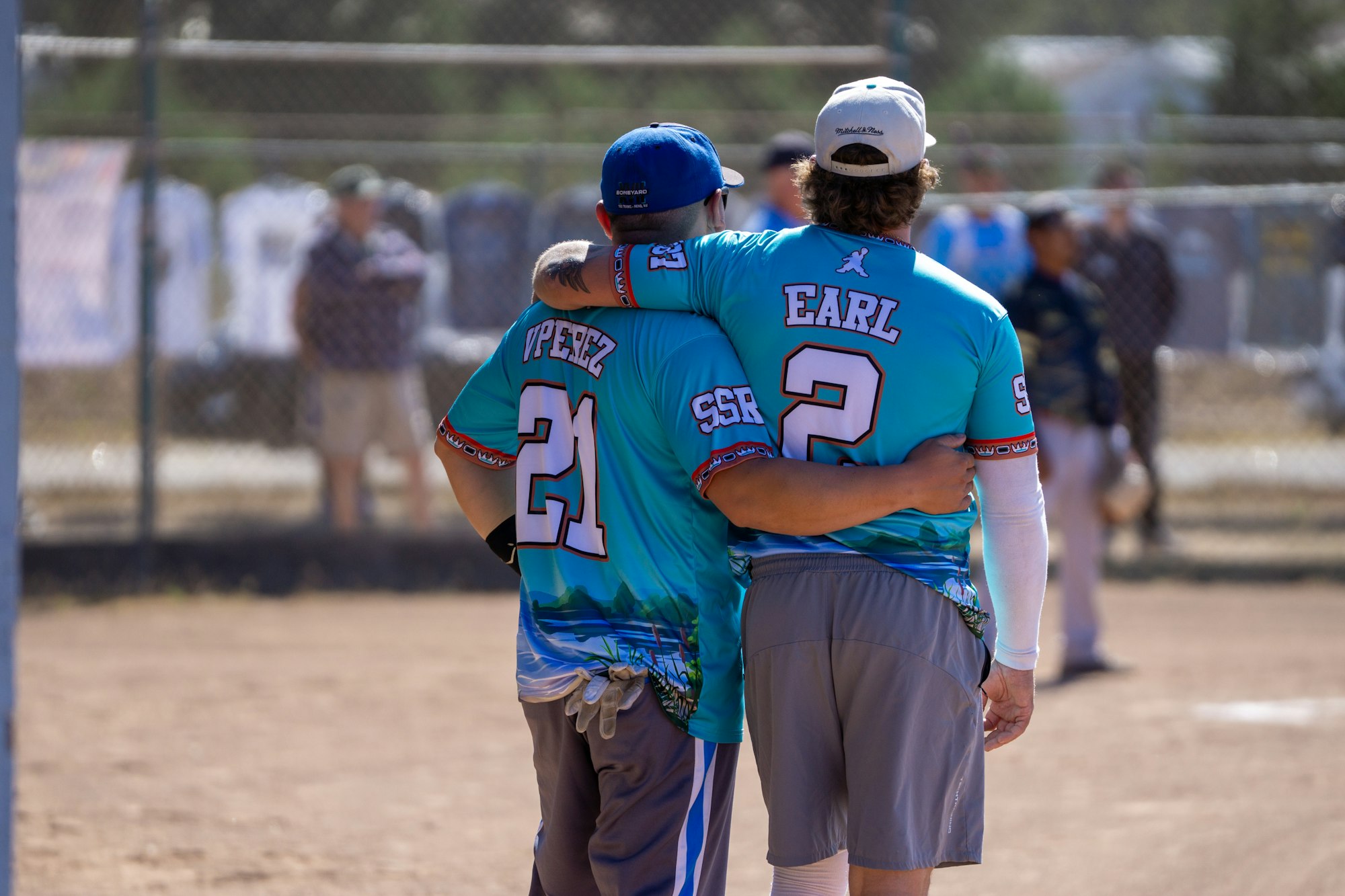 Two people in blue jerseys with numbers 21 and 2, arm-in-arm on a baseball field.
