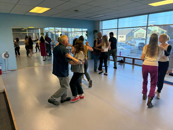 A dance class in a studio with participants dancing with partners, reflecting a lively atmosphere.