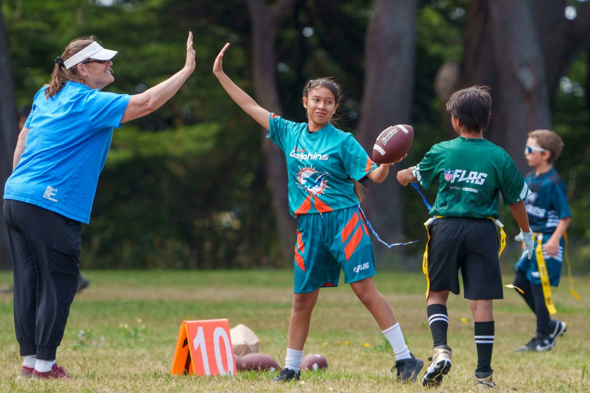 Kids playing flag football, one giving a high five, with others in the background.