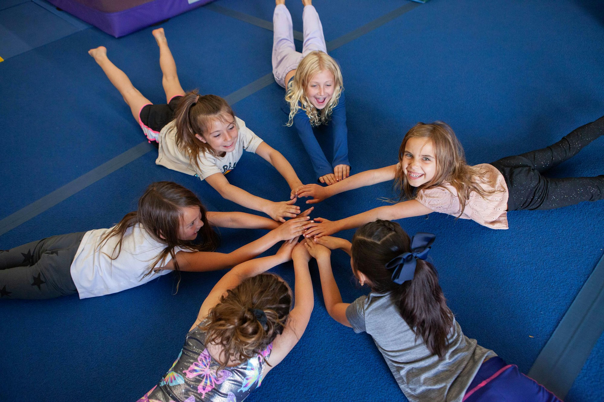 A group of kids lying on the floor together, smiling, and touching hands in the center.