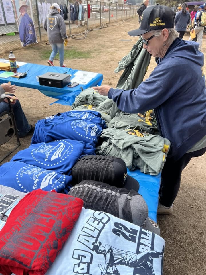 A person is browsing T-shirts and caps on a merchandise table at an outdoor event.