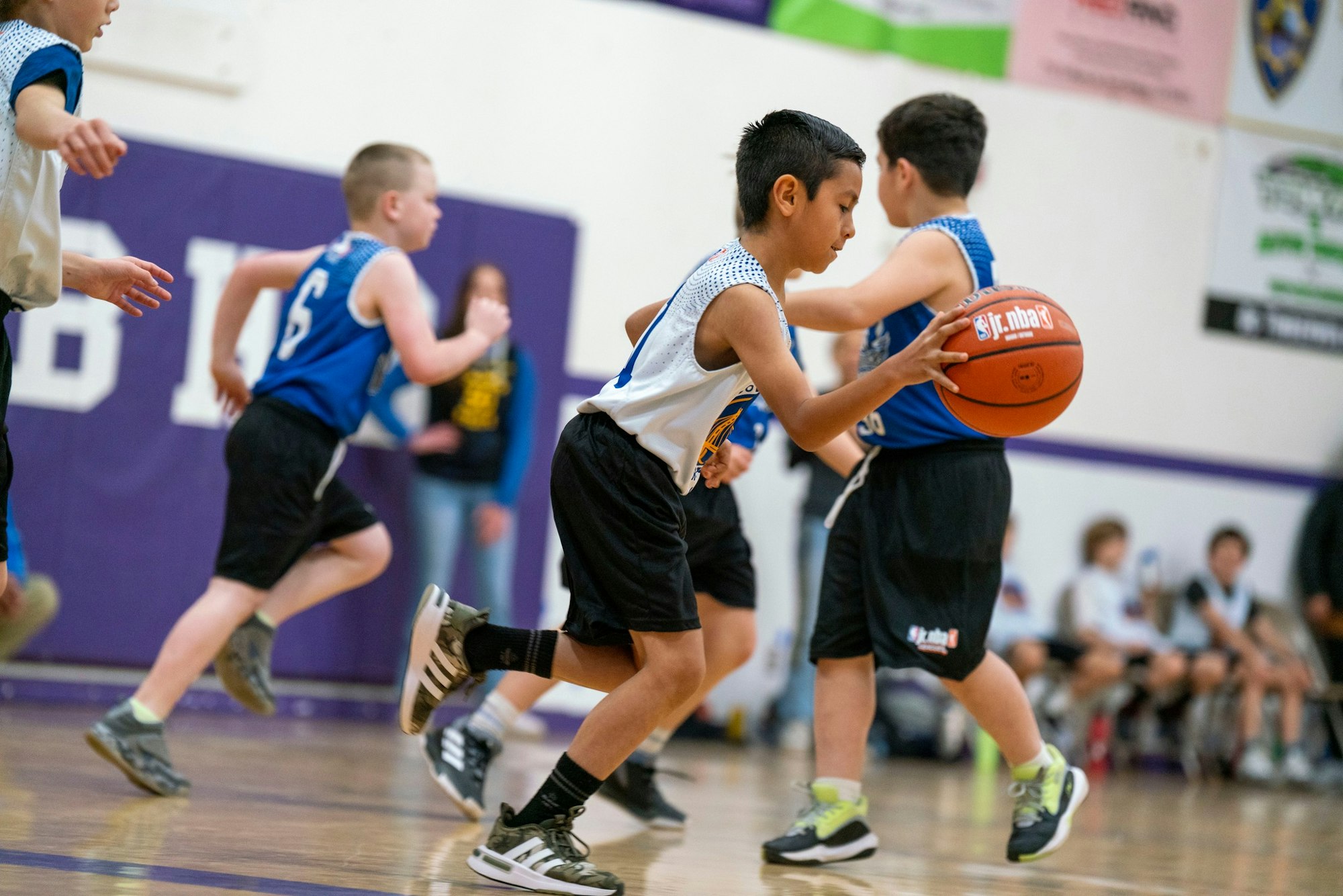 Kids playing a basketball game indoors, one dribbling the ball in action.