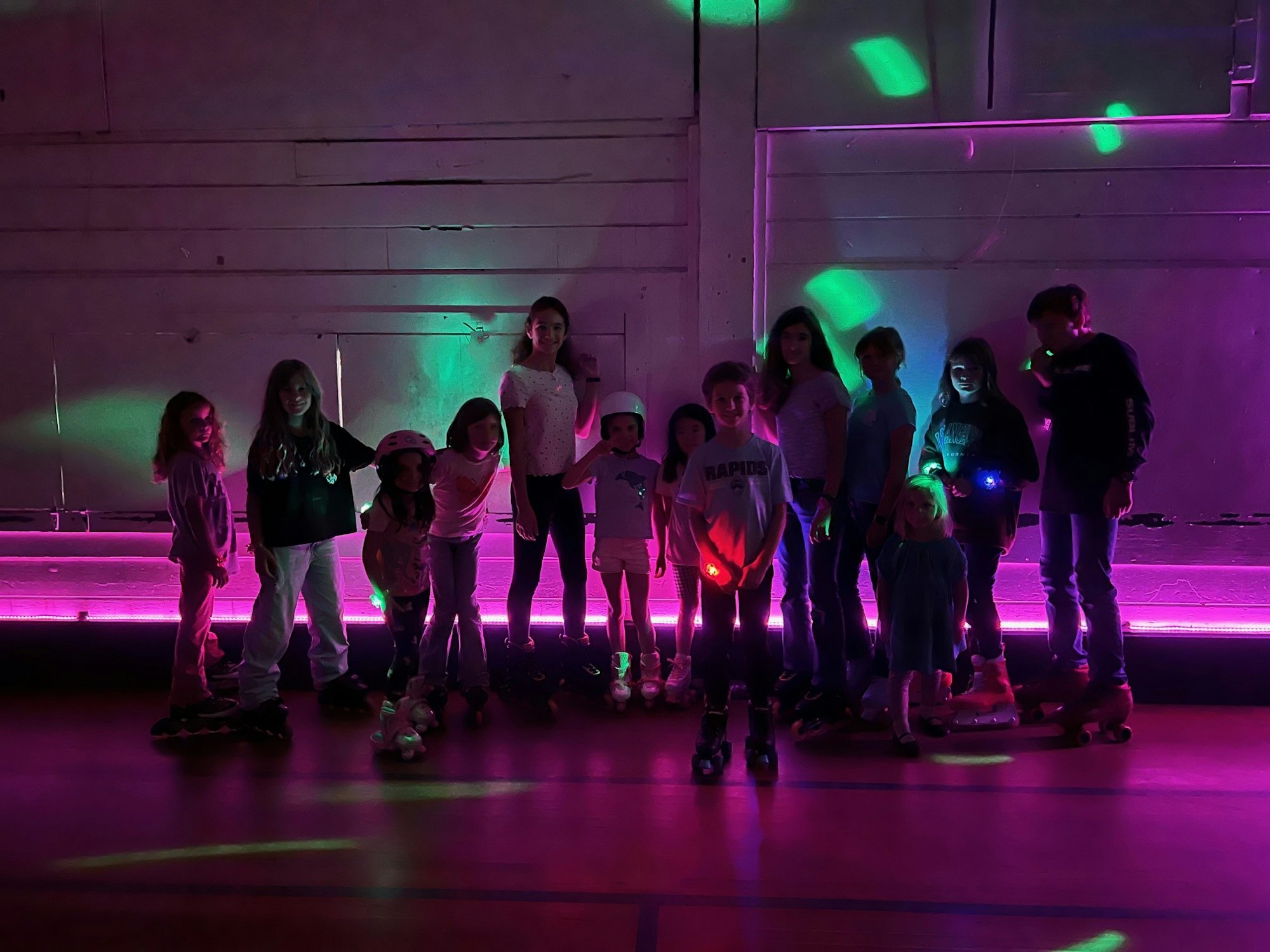 A group of people roller skating in a dimly lit rink with colorful lights.