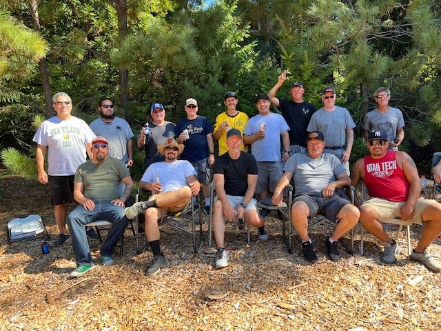 A group of people posing together outdoors, some seated and some standing, in a wooded area.