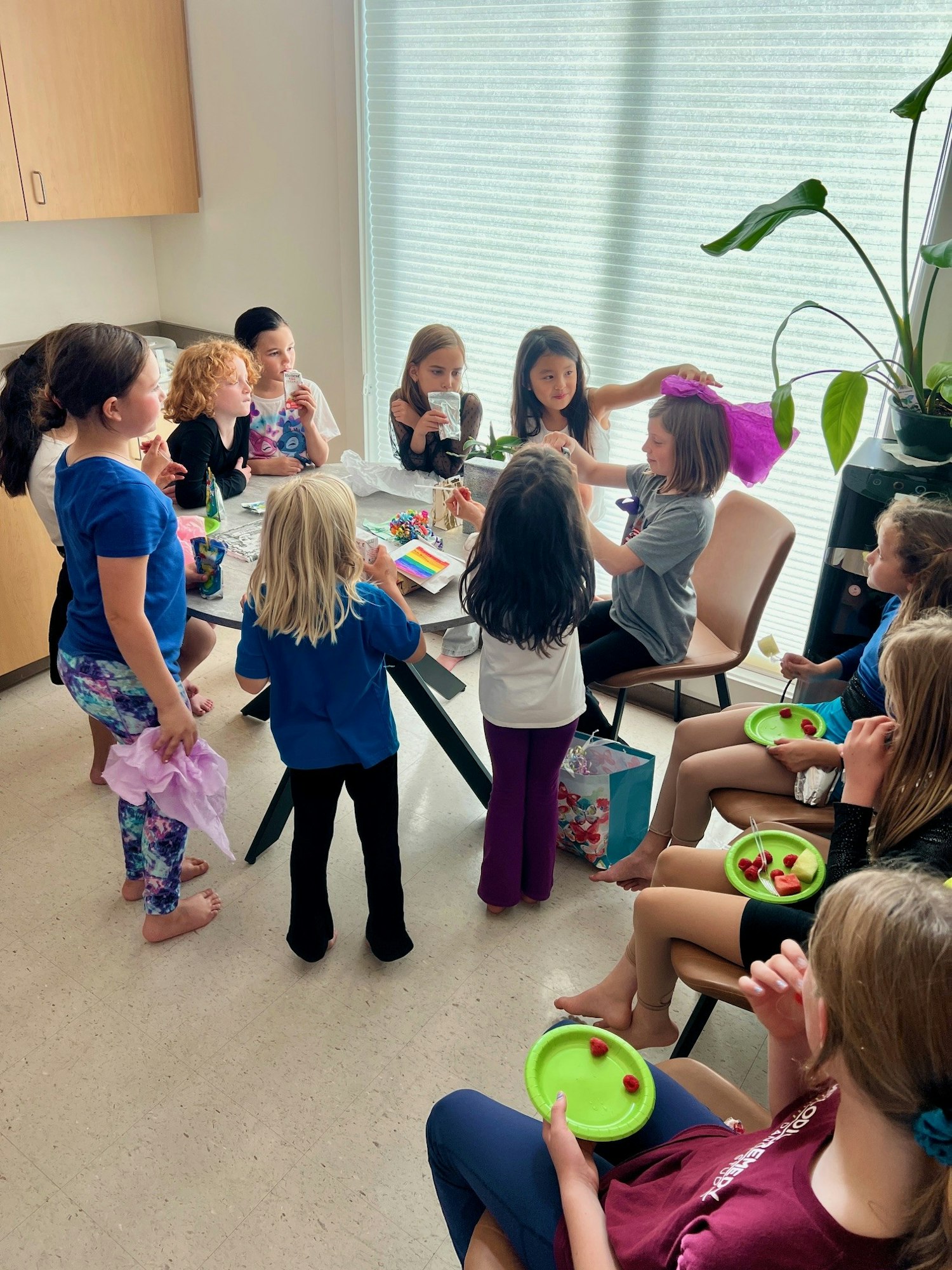 A group of children gathered indoors, enjoying snacks and crafts around a table.